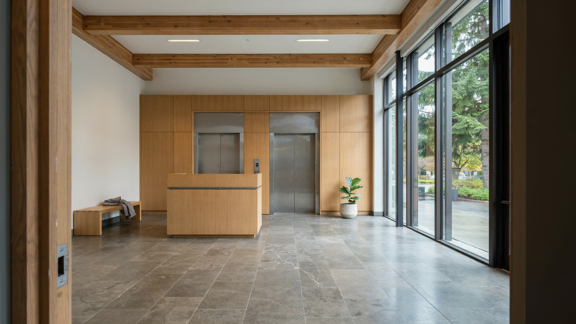 A bright multi-tenant office building lobby with stone floors and a tall glass facade