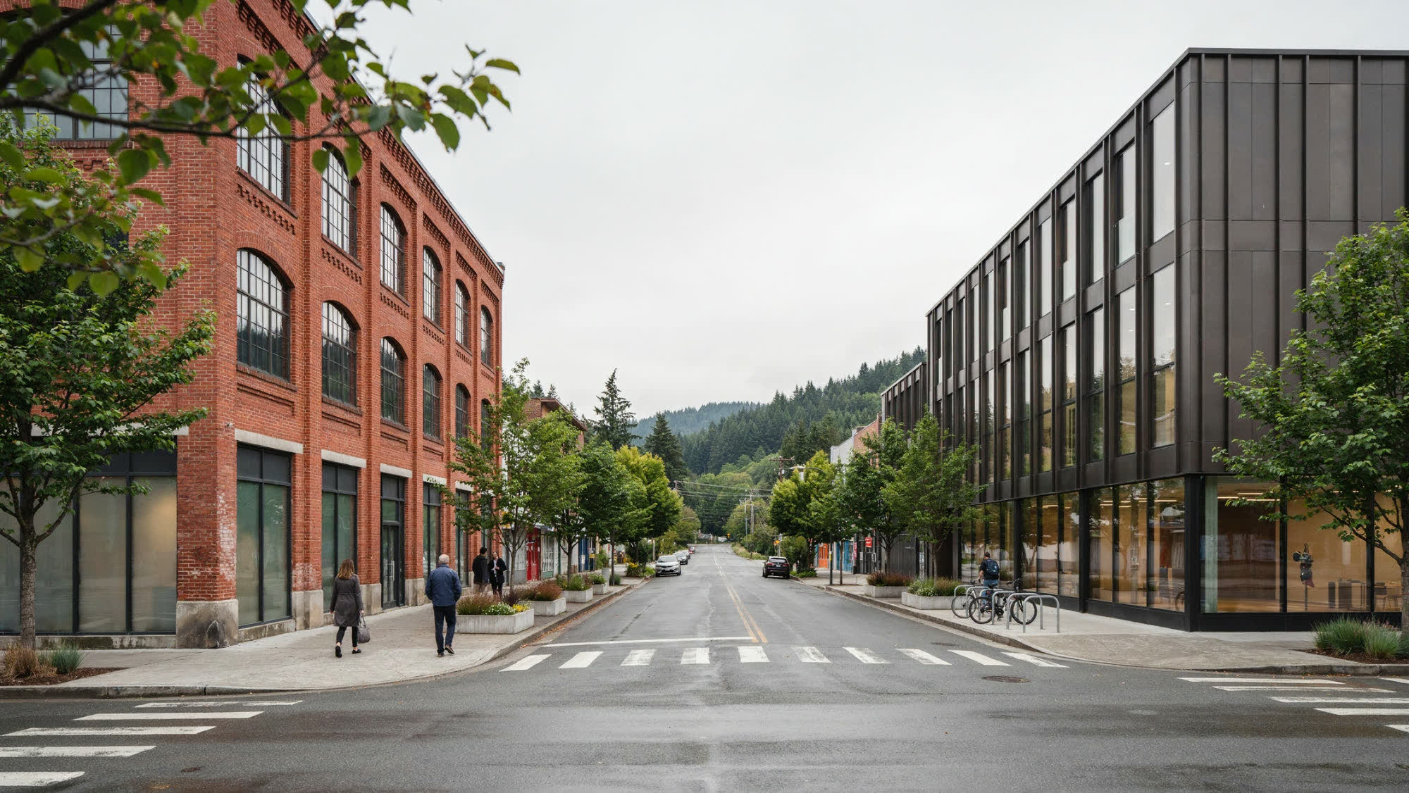 A mid-rise commercial street with brick and metal-clad buildings and forested hills beyond