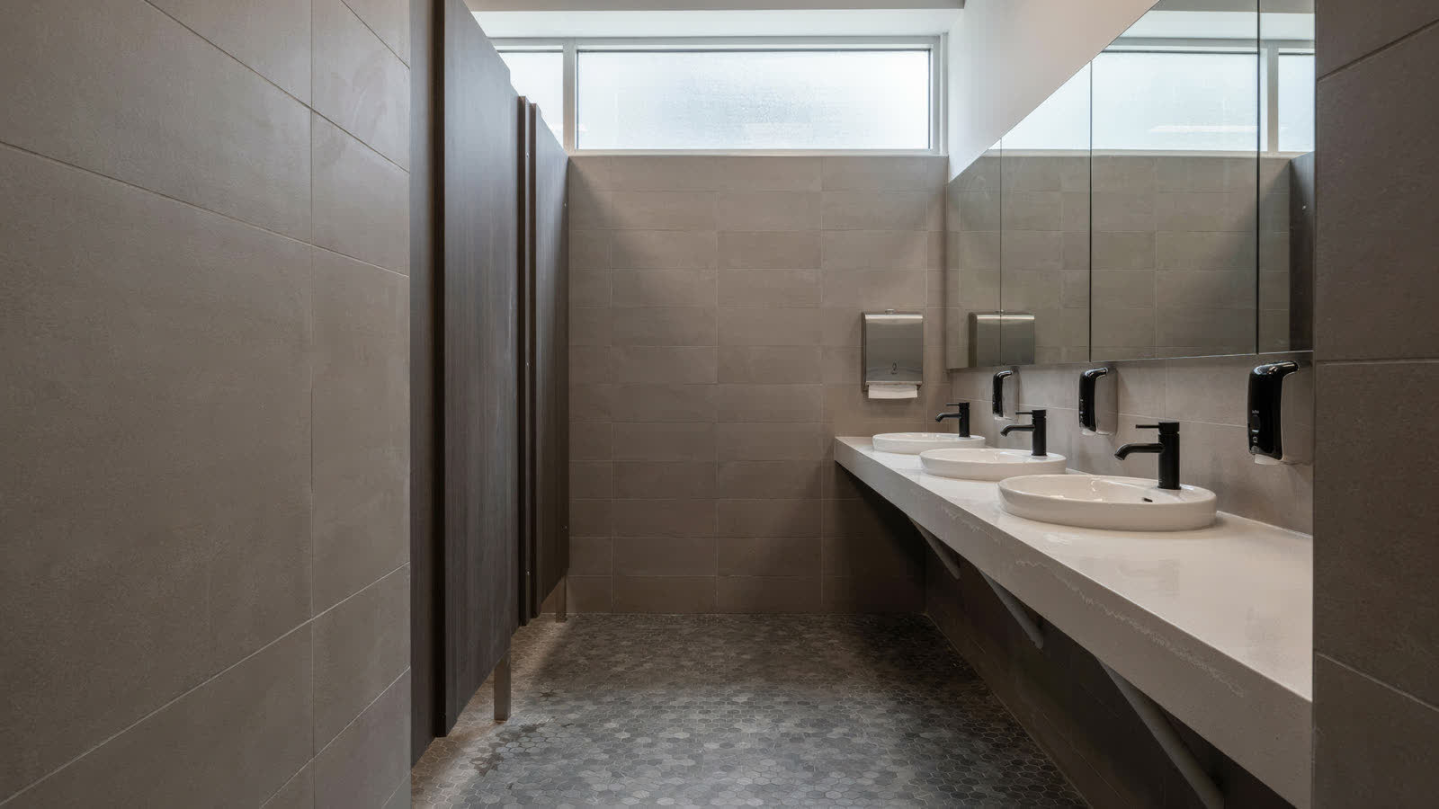 A commercial restroom with gray tile and matte black fixtures
