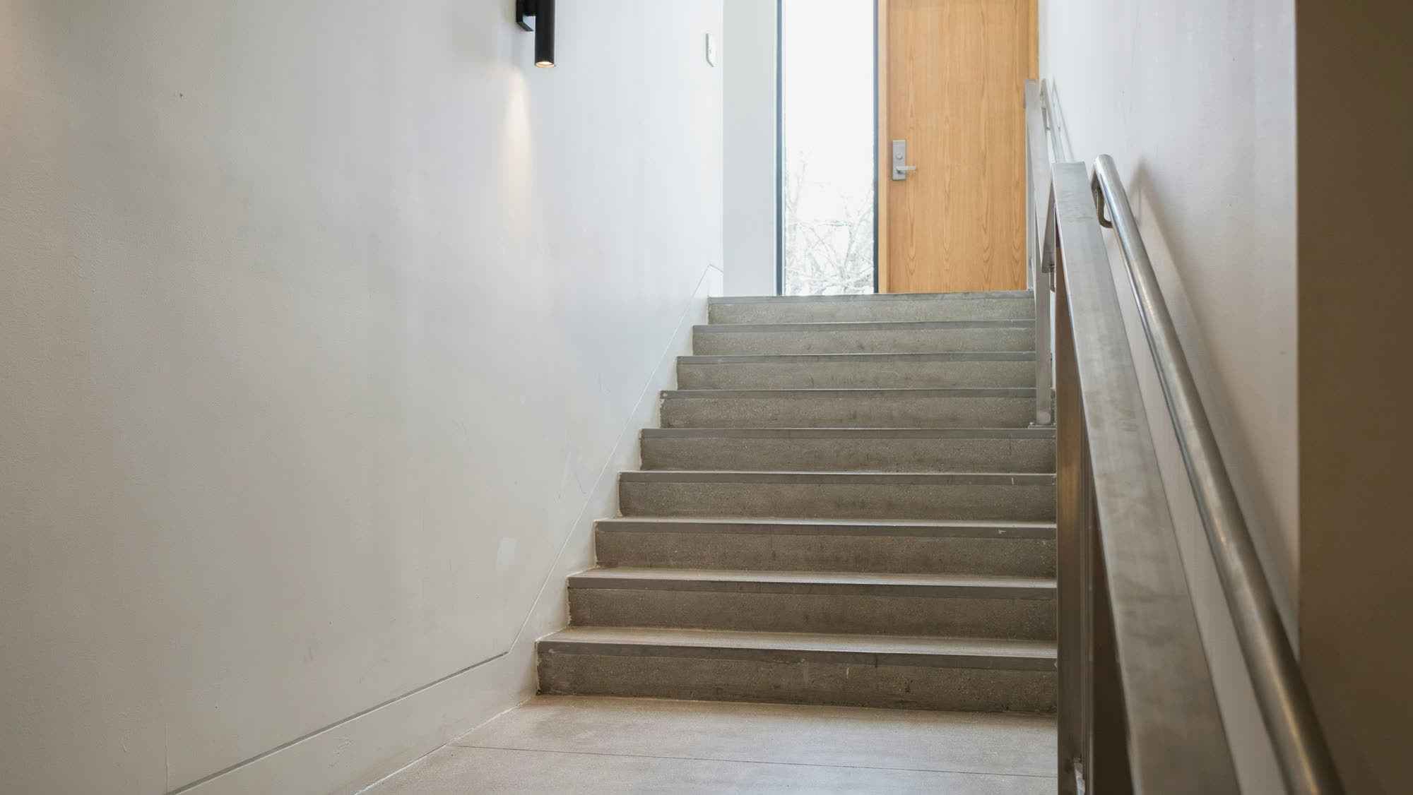 A commercial stairwell with a stainless steel handrail and concrete treads