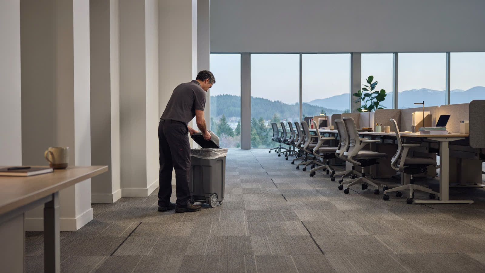 A janitorial team member emptying a recycling bin in an open office after hours
